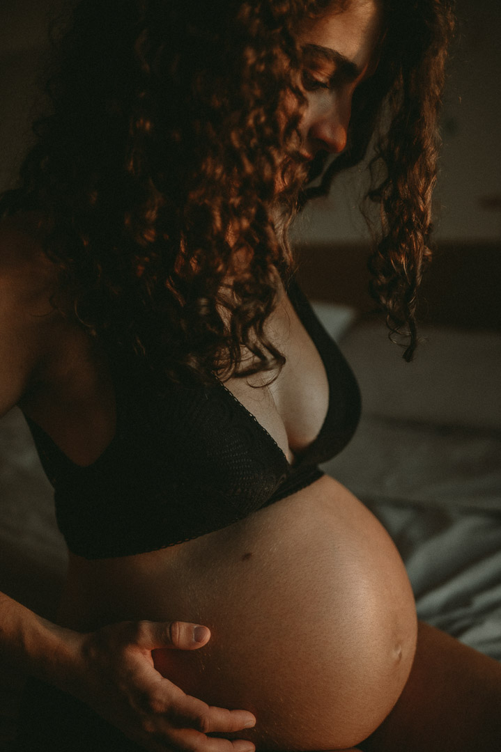 Schwangere sitzt auf Bettkante und betrachtet ihren Babybauch