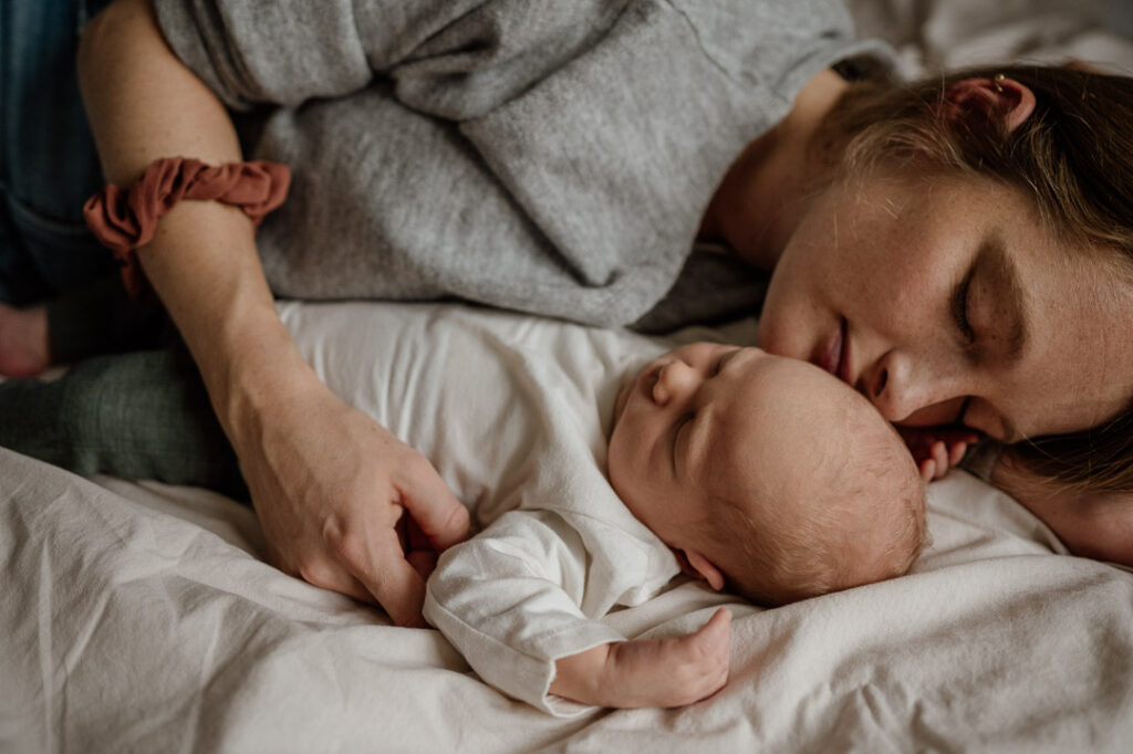 Baby liegt im Arm von Mama auf dem Bett