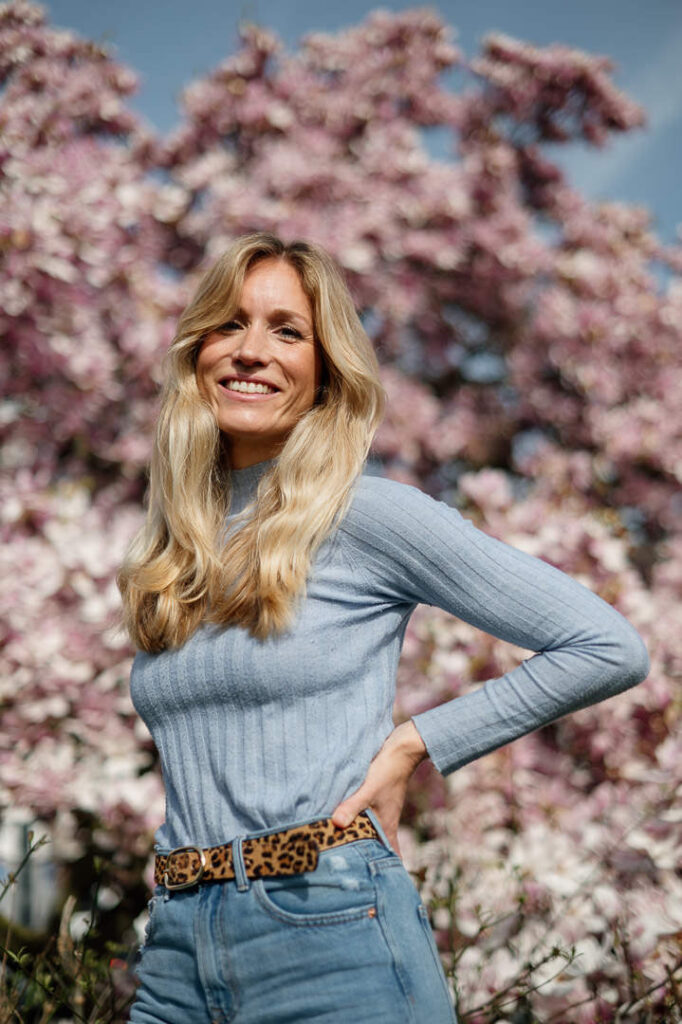 Blonde Frau steht vor Blumen und strahlt