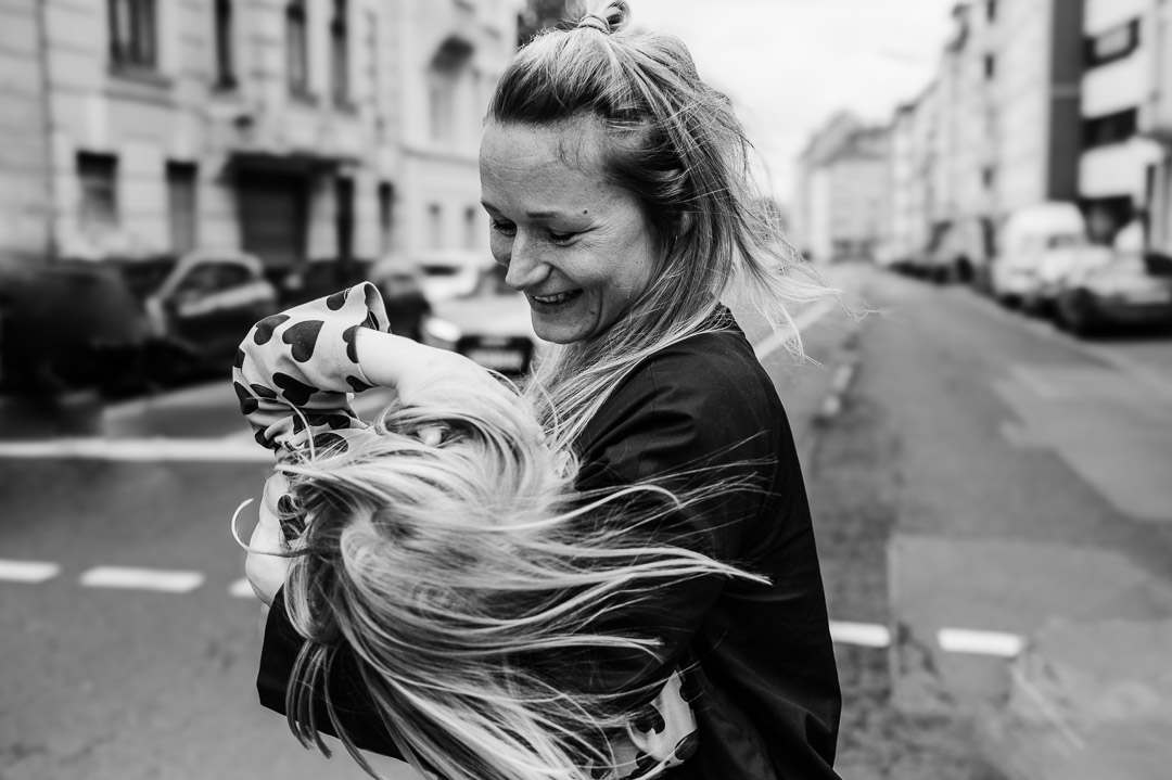 Mama trägt Kind über Straße mit wehenden Haaren