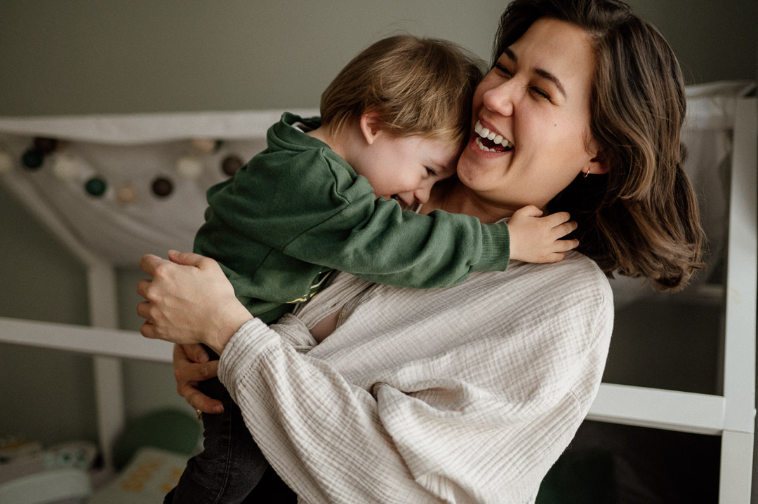 Lachende Mama mit Kleinkind auf dem Arm