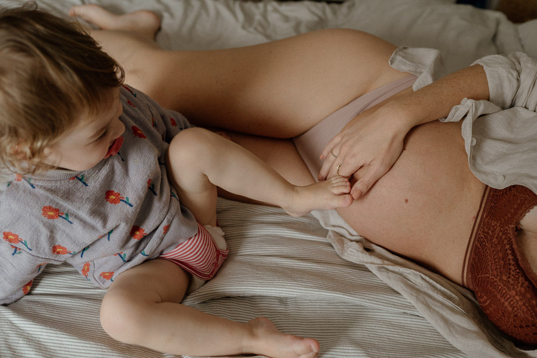 Kleinkind hält seinen Fuss an den Babybaucb seiner Mama