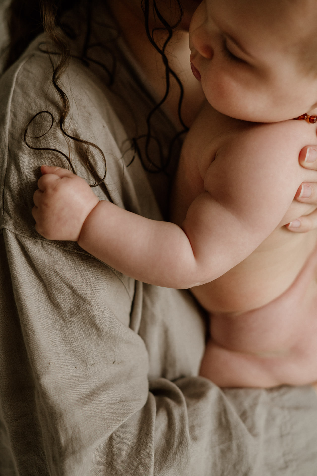 Baby im Arm der Mama spielt mit ihren Haaren
