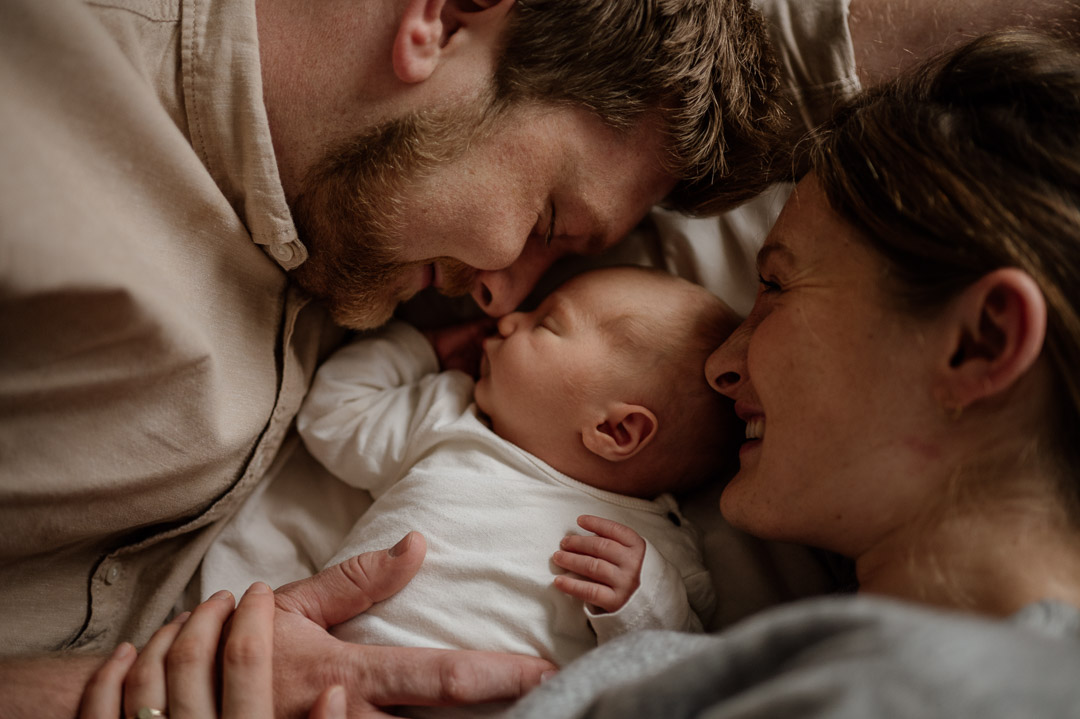 Baby liegt gekuschelt zwischen Papa und Mama auf dem Bett